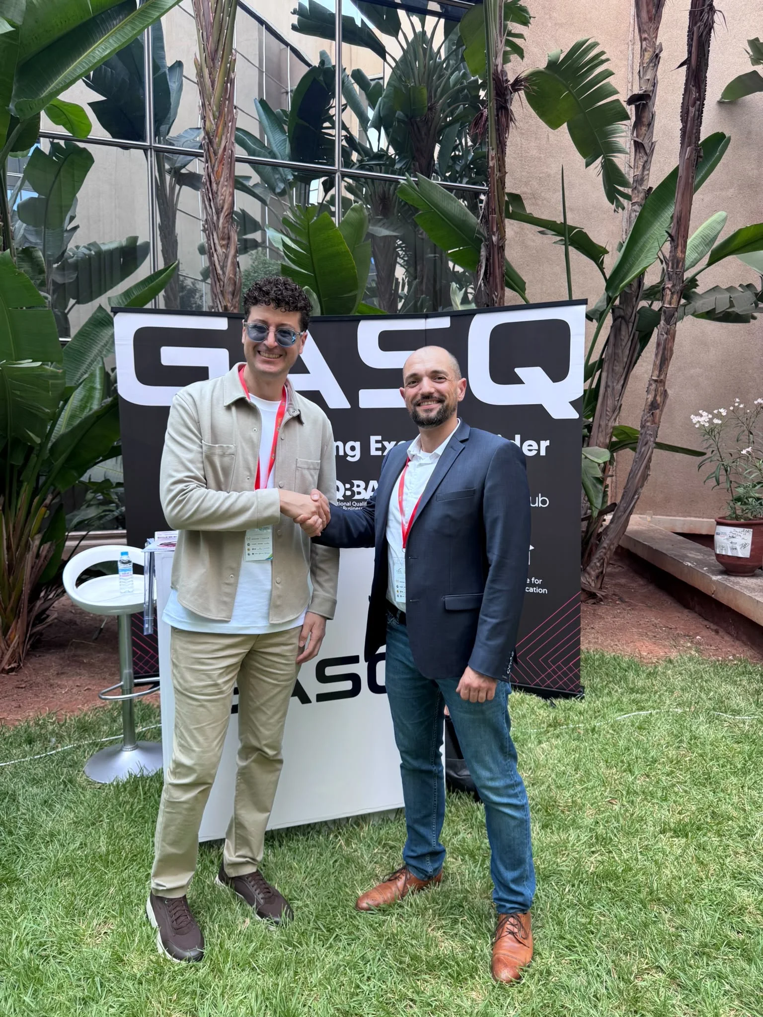 Deux participants se serrent la main devant le stand GASQ, dans le jardin du Technopark.