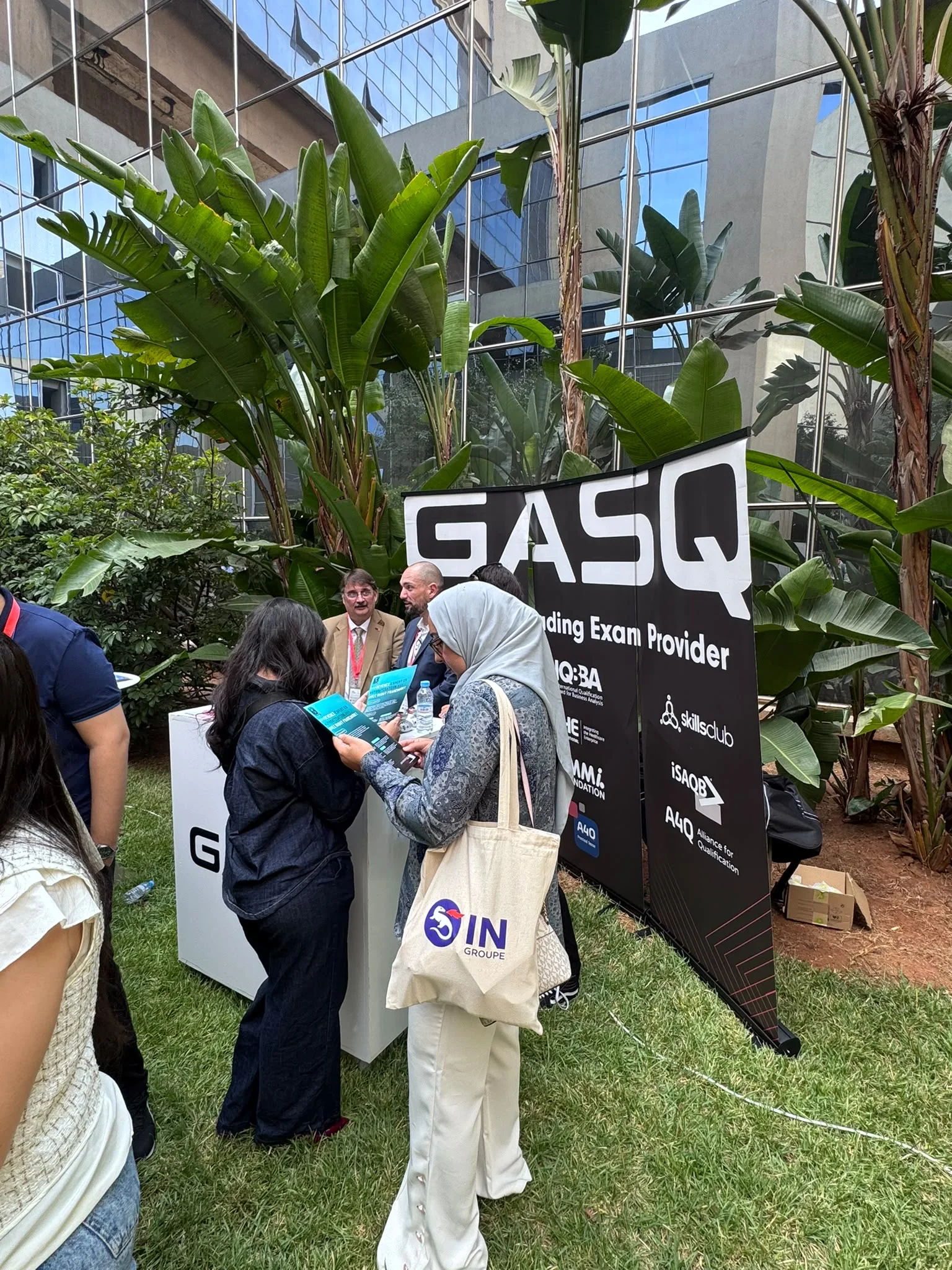 Des visiteurs discutent devant un stand et une grande bannière GASQ entourée de plantes.