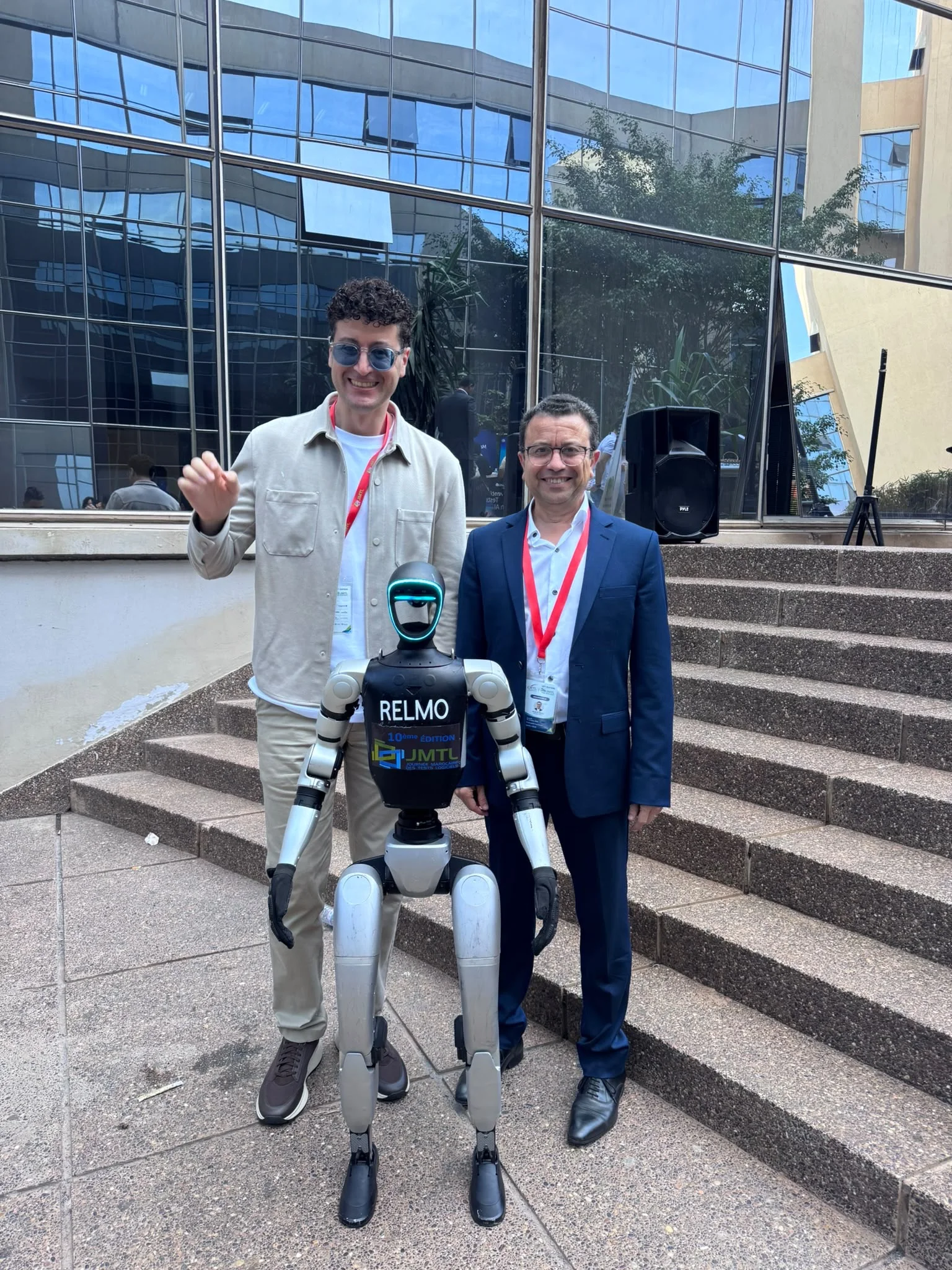 Deux participants posent avec un robot portant le logo de la 10ᵉ édition de la JMTL.
