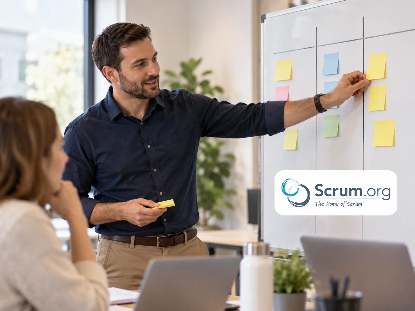 Facilitateur organisant le flux de travail sur un tableau Kanban, avec le logo Scrum.org.